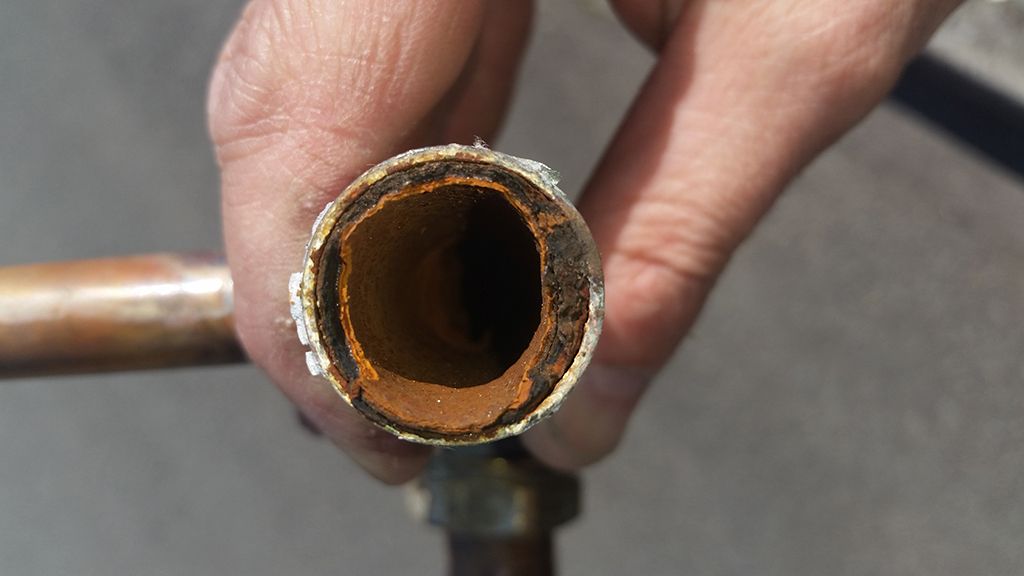 Photo showing a pipe that is corroded and clogged which may be prevented by power flushing the system
